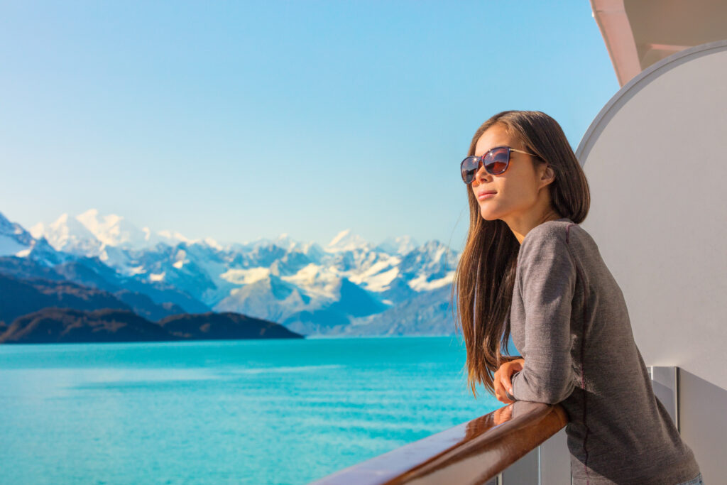 Woman in sunglasses looking out at mountains from the deck of an Alaskan cruise ship