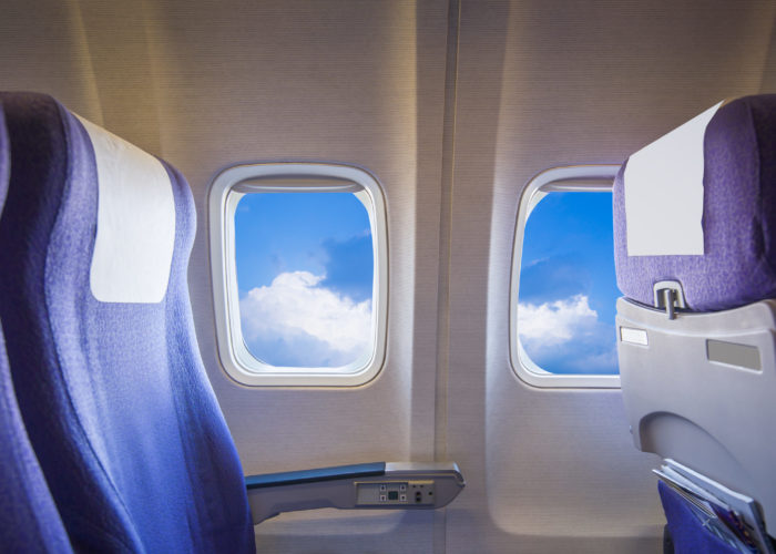 Empty row of plane seats with blue sky as seen out the window