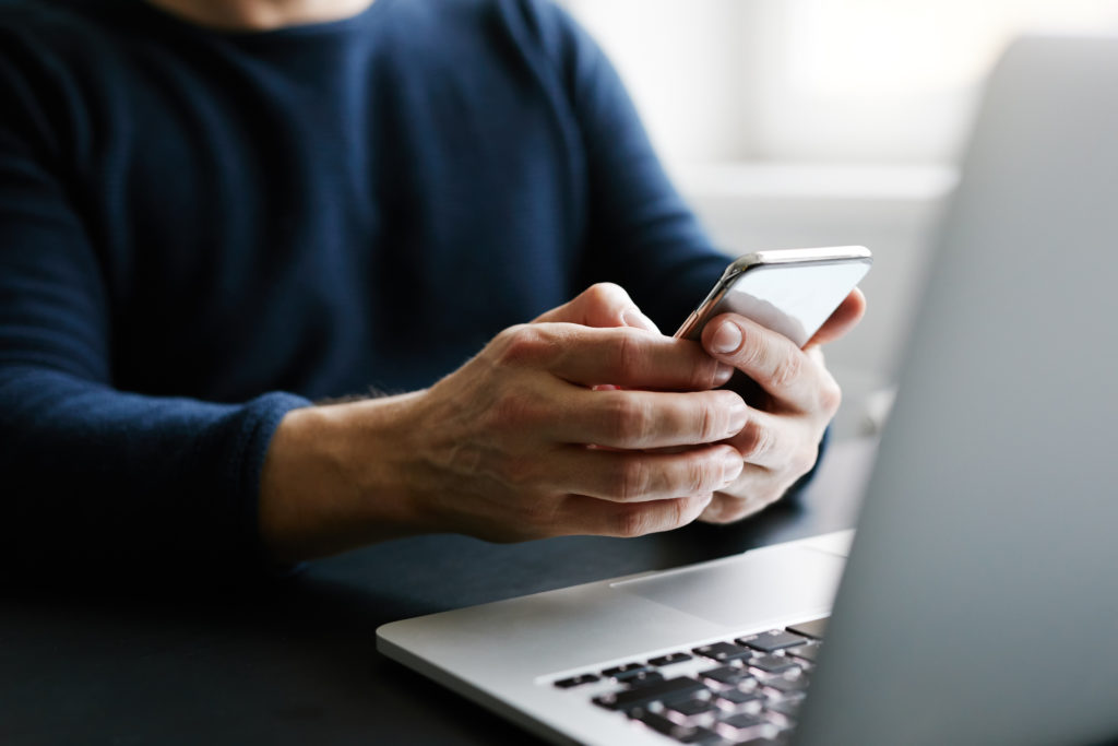 Close up of person using smartphone while on laptop