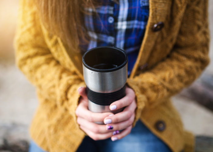 Woman holding hot travel mug of coffee