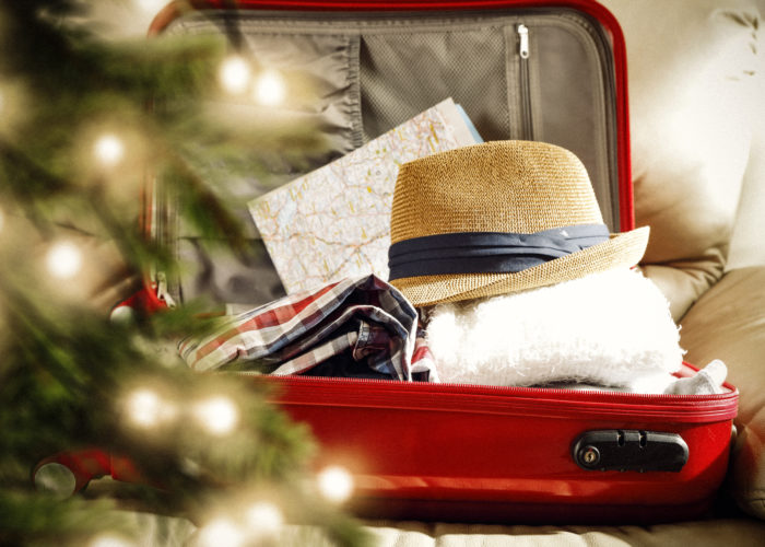 Suitcase packed with travel gear in background with blurry Christmas tree in foreground