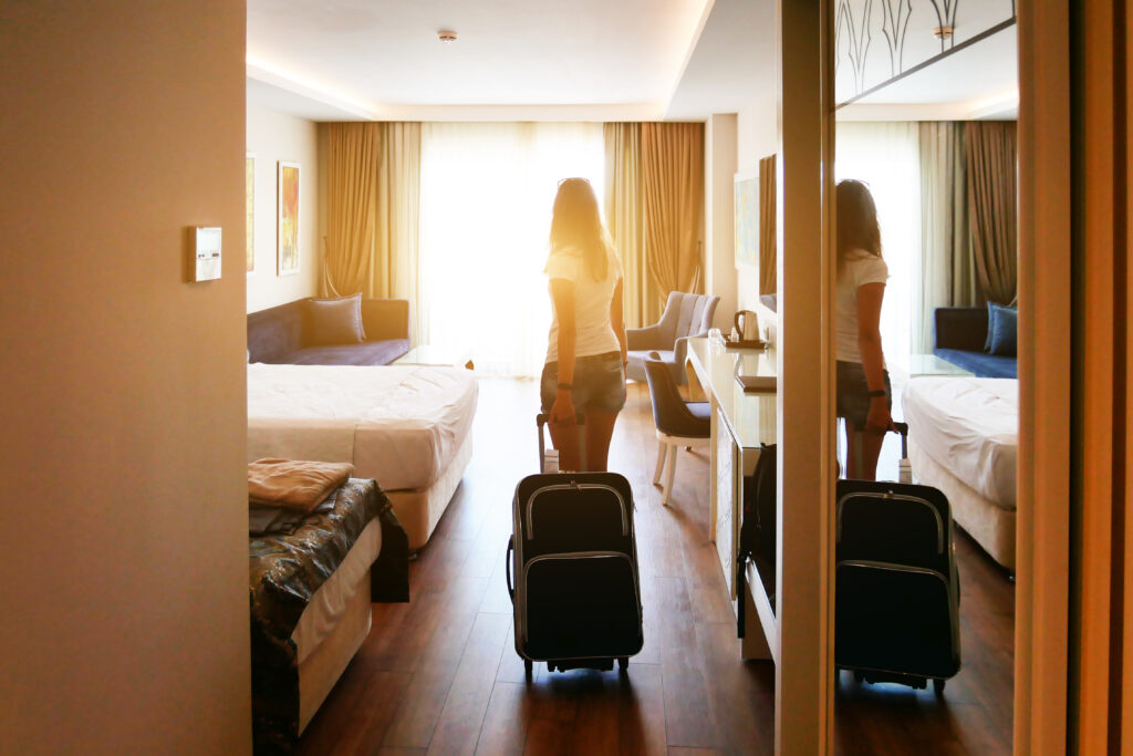 Woman walking into hotel room with rolling suitcase, backlit by the sun