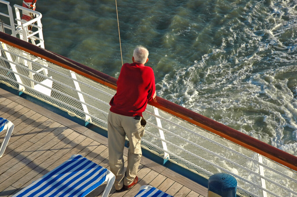Elderly man looking out over the ocean standing on the deck of a cruise ship