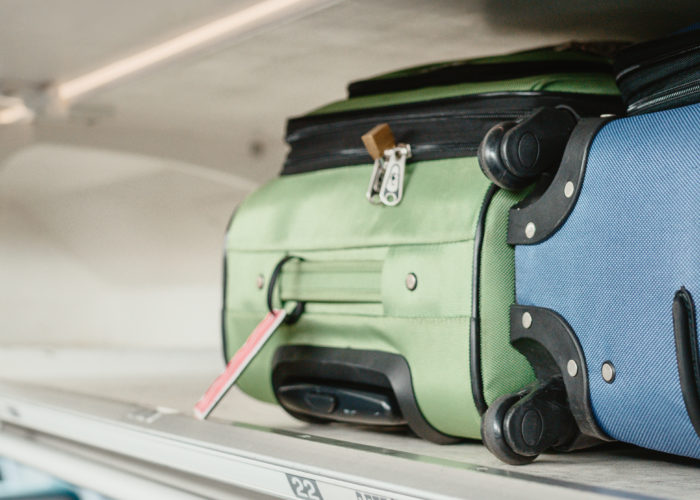 Two suitcases, one green and one blue, in the overhead bin of an airplane
