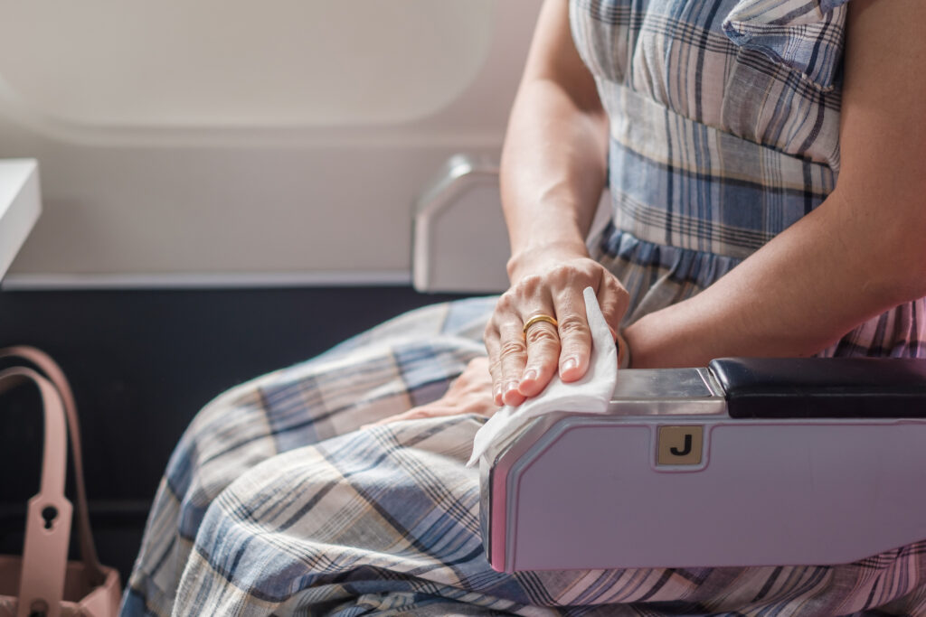 Close up of person in a dress wiping down armrest of an airplane seat with a sanitizing wipe