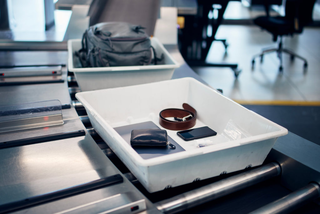 Bin on airport security conveyor belt with person's wallet, electronics, and belt