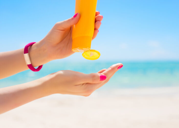 Close up of person squeezing sunscreen from an orange bottle into their open hand at the beach