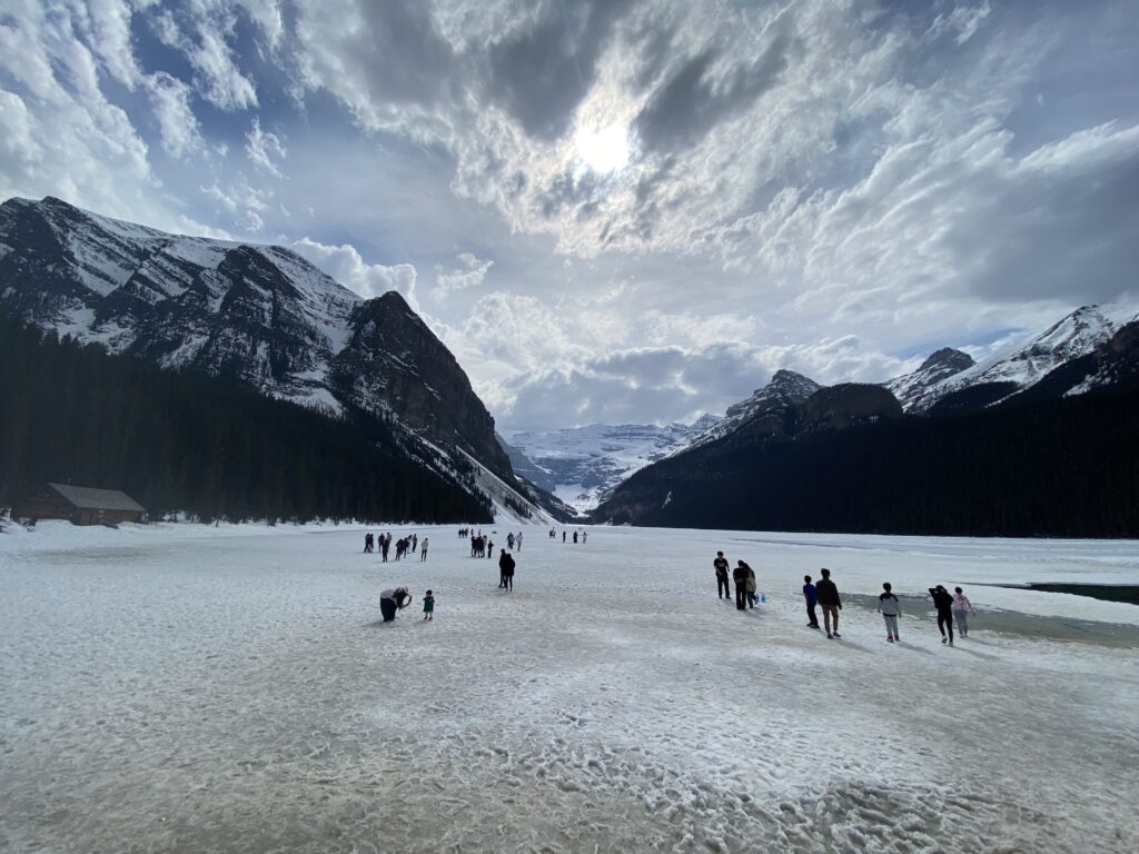 People walking around the frozen landscape of Lake Louise with mountains in the background